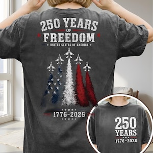 May include: A charcoal grey t-shirt featuring a back graphic with five fighter jets leaving red, white, and blue smoke trails. Text reads 250 YEARS OF FREEDOM UNITED STATES OF AMERICA 1776-2026. The front chest area displays 250 YEARS 1776-2026.