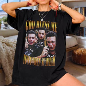 Puede incluir: Camiseta negra con un gráfico dorado que dice "GOD BLESS ME" sobre una foto de tres hombres. Debajo de la foto, el texto dice "IT'S FOREVER SUMMER". La camiseta es de estilo casual.