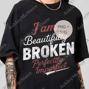 May include: Black t-shirt featuring the text "I am Beautifully Broken Perfectly Imperfect" in white and red. The shirt has a round neck and short sleeves. A gold chain is visible at the neckline.