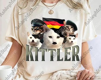 May include: White t-shirt featuring a graphic of several cats wearing hats and a German flag. One cat has a mustache. The word "KITTLER" is printed in large letters below the cats.