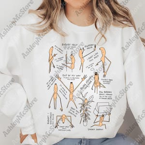May include: White sweatshirt with a quirky cartoon design. The illustrations show stick figures in various poses with phrases like "Robert Help" and "You're ruining the vibe". The design has a humorous theme.