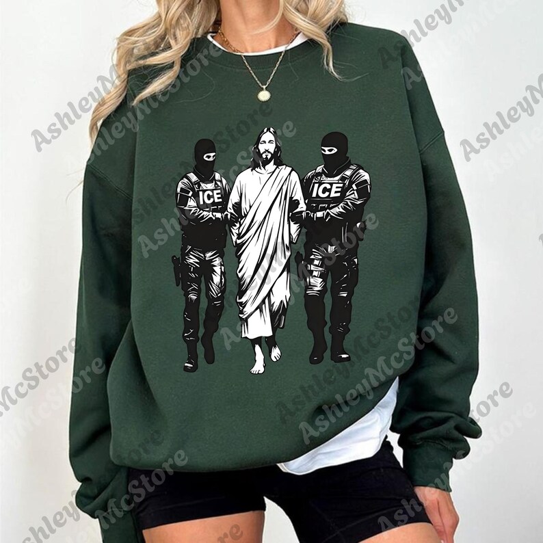 K&ouml;nnte beinhalten: Dunkelgr&uuml;nes Sweatshirt mit einem schwarz-wei&szlig;en Grafikdruck. Die Grafik zeigt Jesus zwischen zwei Figuren in taktischer Ausr&uuml;stung, mit dem Text "ICE" auf ihren Uniformen.