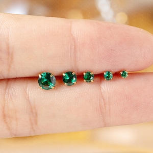 Puede incluir: Un conjunto de cinco pendientes de oro con gemas de color verde esmeralda. Los pendientes varían en tamaño, mostrando un diseño graduado. Las gemas son de corte redondo y están engastadas en una montura de oro, creando un aspecto clásico y elegante.