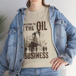 May include: A beige t-shirt featuring a brown graphic of an oil rig and the text "Welcome to the Oil Business".