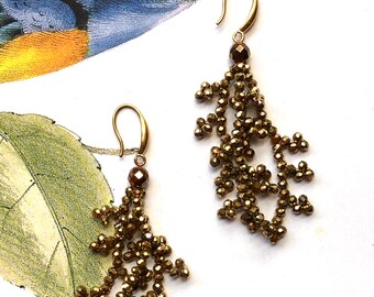 May include: A pair of gold-toned earrings with dangling, beaded tassels. The beads are small and have a metallic sheen.