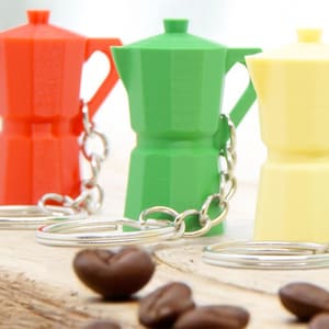 May include: Four colorful miniature coffee pot keychains. The keychains are red, green, yellow, and light blue. Each keychain has a silver metal ring and chain.