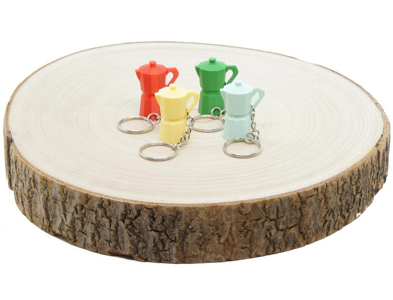 K&ouml;nnte beinhalten: Vier bunte Miniatur-Kaffeekannen-Schl&uuml;sselanh&auml;nger auf einer Holzoberfl&auml;che. Die Schl&uuml;sselanh&auml;nger sind rot, gr&uuml;n, gelb und blau.
