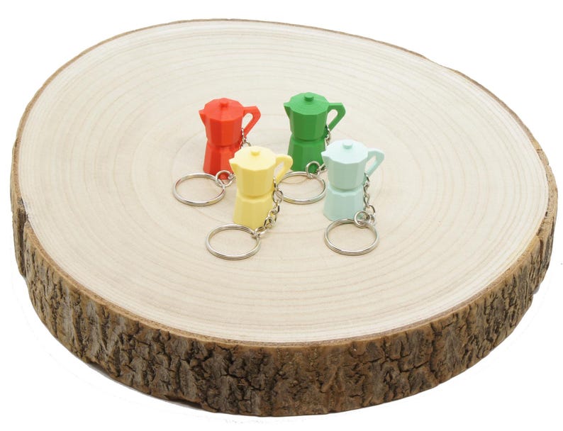 K&ouml;nnte beinhalten: Vier bunte Miniatur-Kaffeekannen-Schl&uuml;sselanh&auml;nger auf einer Holzoberfl&auml;che. Die Schl&uuml;sselanh&auml;nger sind rot, gr&uuml;n, gelb und blau.