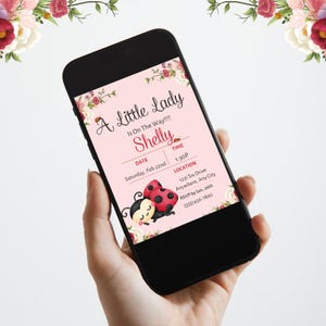May include: A smartphone displays a baby shower invitation with the text "A Little Lady Is On The Way!!!" and the name "Shelly." The invitation features ladybug illustrations and floral accents. The date is Saturday, Feb 22nd, at 1:30 PM.