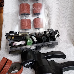 May include: A collection of Stampin' Around craft supplies including two black plastic handle tools with the text stampin' around, a clear plastic tray containing six cylindrical rubber stamps with various patterns, and several black ink cartridges.