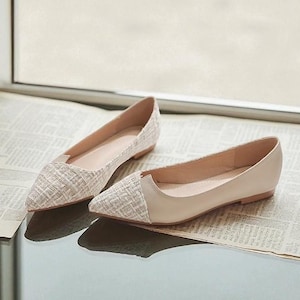 May include: A pair of beige and white flats with pointed toes. One shoe has a textured, woven design on the toe, while the other has a smooth, solid beige toe. The shoes are displayed on a newspaper.
