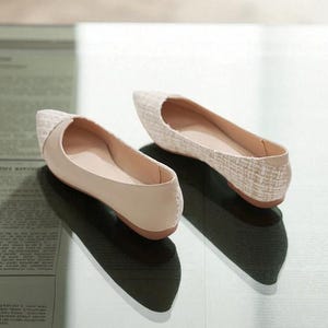 May include: A pair of beige ballet flats with a pointed toe. The toe box has a woven texture, while the rest of the shoe is smooth. The shoes are displayed on a light-colored surface.