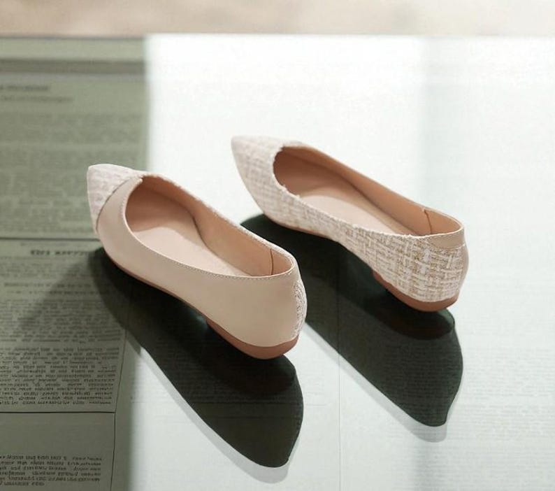 May include: A pair of beige ballet flats with a pointed toe. The toe box has a woven texture, while the rest of the shoe is smooth. The shoes are displayed on a light-colored surface.