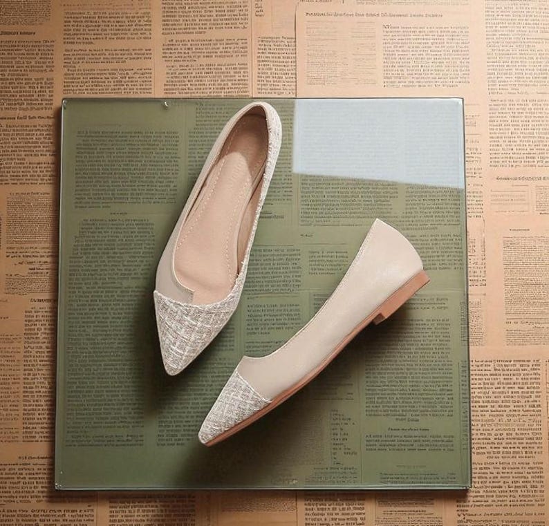 May include: A pair of beige flats with a pointed toe and a woven texture on the toe cap. The shoes are displayed on a glass surface with a green tint, set against a backdrop of vintage newspaper clippings.