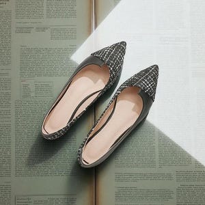 May include: A pair of black and white patterned flats with pointed toes. The shoes have a black leather trim and a light pink interior. The flats are displayed on a vintage newspaper background.