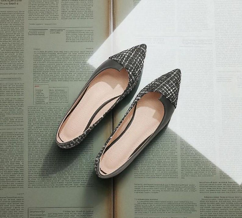 May include: A pair of black and white patterned flats with pointed toes. The shoes have a black leather trim and a light pink interior. The flats are displayed on a vintage newspaper background.
