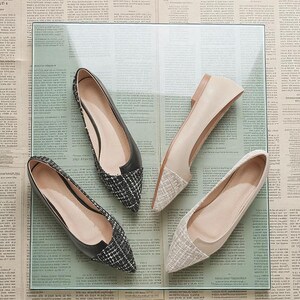 May include: Four pairs of women's flats in a variety of styles. Two pairs have black leather uppers with a black and white tweed toe. The other two pairs are beige with a tweed toe. The shoes are displayed on a glass surface.