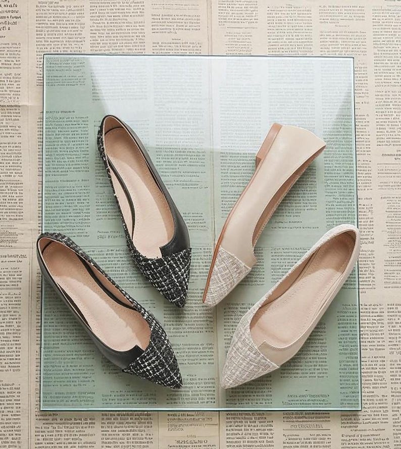 May include: Four pairs of women's flats in a variety of styles. Two pairs have black leather uppers with a black and white tweed toe. The other two pairs are beige with a tweed toe. The shoes are displayed on a glass surface.