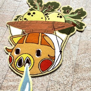May include: A whimsical, handmade rug featuring a cartoon pig design with a brown basket of yellow fruit and green leaves. The pig has orange, yellow, and red accents, with a blue and white teardrop shape below. The rug is placed on a tiled floor.