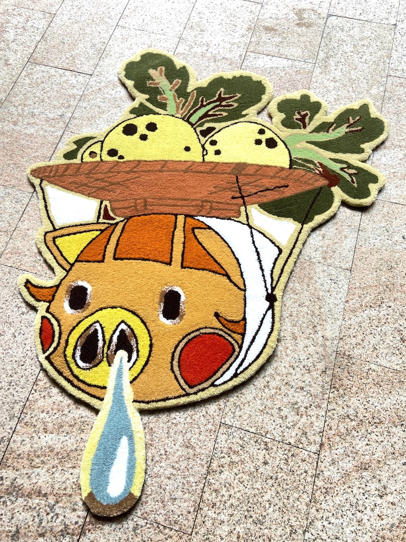 May include: A whimsical, handmade rug featuring a cartoon pig design with a brown basket of yellow fruit and green leaves. The pig has orange, yellow, and red accents, with a blue and white teardrop shape below. The rug is placed on a tiled floor.