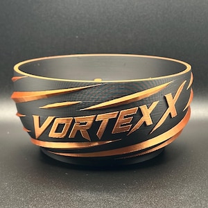May include: A matte black bowl featuring a copper-colored spiral design wrapping around the exterior. The word VORTEXX is embossed in copper lettering on the front, integrated into the swirling pattern that encircles the entire vessel.