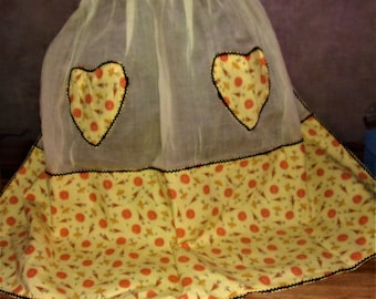 May include: A yellow and orange vintage apron with a sheer overlay and two heart-shaped pockets. The apron has a black trim and a pattern of small orange and yellow flowers.