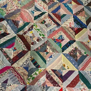 May include: A patchwork quilt featuring a variety of fabric scraps in numerous colors and patterns, including floral, plaid, striped, and cartoon prints. The quilt is constructed from square blocks, each composed of multiple diagonal fabric strips.