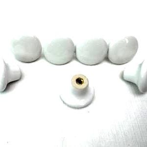 May include: A collection of white ceramic cabinet knobs. The knobs are round with a glossy finish, and some have a brass-colored screw. The knobs are arranged on a white surface.