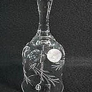 May include: A clear glass bell with a long handle and a flared base. The bell features etched floral designs and a small, round sticker. The clapper is visible inside. The bell is likely a decorative item.