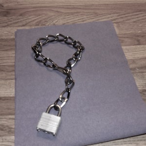 May include: A silver chain with a silver padlock attached. The chain is looped into a circle and the padlock is hanging from the bottom of the chain.
