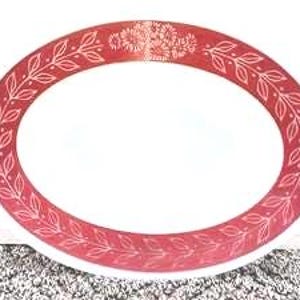 May include: An oval serving platter with a white center and a wide red border. The red border features a continuous white line drawing of a leafy vine pattern and a cluster of flowers at the top center of the rim, creating a decorative frame.