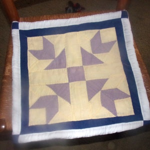 Puede incluir: Un cojín de silla acolchado blanco y azul con un patrón de estrella morado y amarillo.