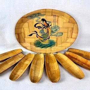 May include: A bamboo serving tray with a painted illustration of a woman in a flowing dress, surrounded by clouds and water. The tray is accompanied by seven wooden serving dishes, each with a curved, boat-like shape.