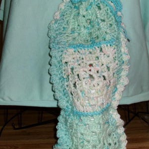 Op de afbeelding: Een handgehaakt item in tinten blauw, wit en een vleugje roze. Het heeft een geschulpte rand en een trekkoordsluiting. Het open haakpatroon geeft een textuur. Het is waarschijnlijk een kleine tas of etui.