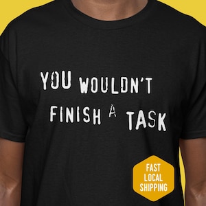 May include: Black t-shirt with the white text "YOU WOULDN'T FINISH A TASK". A yellow hexagon with the words "FAST LOCAL SHIPPING" is in the lower right corner. The shirt is made of a soft material.
