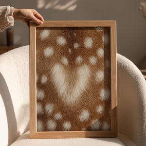 May include: A rectangular wall art print encased in a light-toned wooden frame. The artwork features a high-resolution close-up of brown deer fur with a pattern of white spots and a prominent white heart-shaped patch centred in the middle.