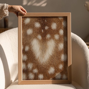 May include: A framed art print featuring a close-up of a deer's coat pattern. The print showcases a brown and white spotted design, with a natural wood frame. The artwork is held by a person's hand, suggesting a focus on home decor.