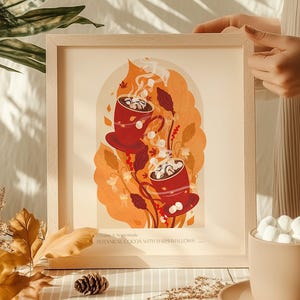 Könnte beinhalten: Gerahmter Kunstdruck mit zwei roten Kakaotassen mit Marshmallows, vor einem orangefarbenen und beigen Hintergrund. Der Druck enthält den Text "Creamy & homemade BOTANICAL COCOA WITH MARSHMALLOWS". Das Kunstwerk befindet sich in einem hellen Holzrahmen.