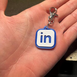 May include: A blue and white keychain with the LinkedIn logo. The keychain has a silver metal clasp.