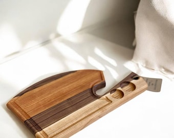 Peut inclure: Planche à découper en bois au design unique. Elle présente des tons de bois clairs et foncés, une section incurvée et une poignée avec trois découpes circulaires. Idéale pour la préparation des aliments, en centimètres.