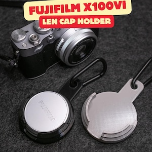 May include: A silver Fujifilm X100VI camera and two lens cap holders with black carabiners. One holder is black and holds a silver Fujifilm lens cap, while the other is light gray. Text in the image reads: FUJIFILM X100VI LEN CAP HOLDER.