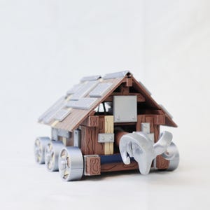 May include: A toy siege ram, featuring a wooden cabin design with a sloped roof and metal accents. The ram has multiple wheels and a silver ram head at the front, designed to simulate a battering ram.