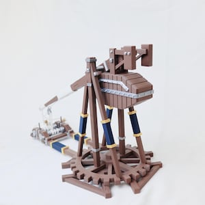 Pode incluir: Modelo de trabuco em madeira castanha com base em forma de engrenagem, detalhes azuis e dourados e funda branca. O modelo apresenta construção detalhada com detalhes metálicos sobre um fundo branco.