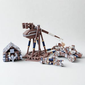 May include: A set of wooden model siege engines, including a trebuchet, catapults, and a battering ram. The models are brown with blue and silver accents, set against a white background.