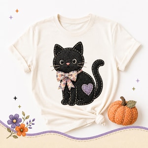Felt black cat with floral bow and purple heart on cream t-shirt.