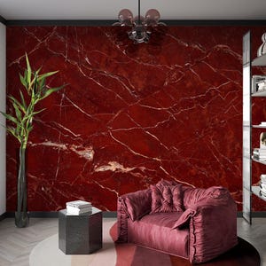 Può includere: Una poltrona imbottita di colore bordeaux con un design capitonné si trova di fronte a un muro di marmo rosso. La poltrona ha una forma grande e arrotondata e uno schienale alto. Il muro di marmo presenta un motivo di venature bianche.