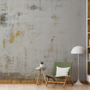 May include: A green chair with a white cushion sits in front of a wall with a distressed, textured, grey and gold paint finish. A white lamp with a round shade stands next to the chair. A small wooden table with a plant on top sits in front of the chair.