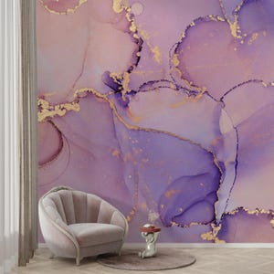 May include: Abstract wall art featuring a purple and gold marble design. The design has a swirling, fluid look with hints of pink and white. The art is displayed on a wall with a pink armchair and a small side table.