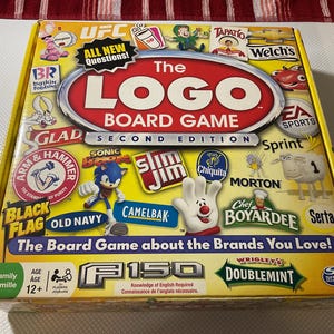 Puede incluir: Caja amarilla del juego de mesa The Logo, Segunda Edición. Muestra logotipos de marcas como UFC, Baskin Robbins, Glad, Sonic y Old Navy. El texto incluye "All New Questions!" y "The Board Game about the Brands You Love!"