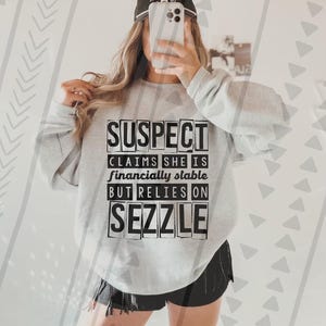 Puede incluir: Una sudadera gris con texto negro que dice "SUSPECT CLAIMS SHE IS financially stable BUT RELIES ON SEZZLE".